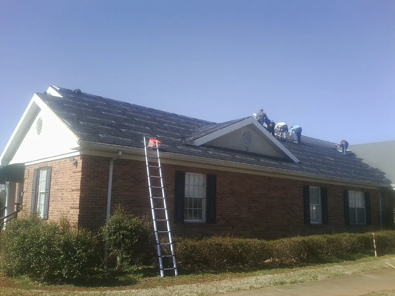 Crew tearing shingles off a brick ranch roof with a ladder set — Metal Roof Repair work by our crew in Fayette