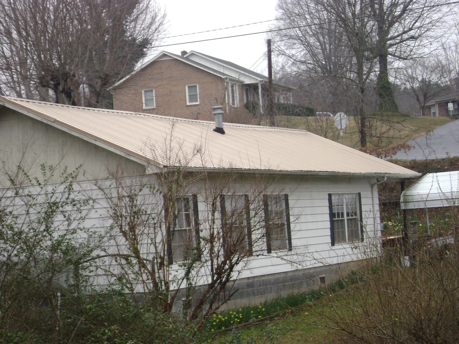 Tan metal roof on a white sided house set into a hillside — Commercial Roofing by Roofing Brothers in Fayette
