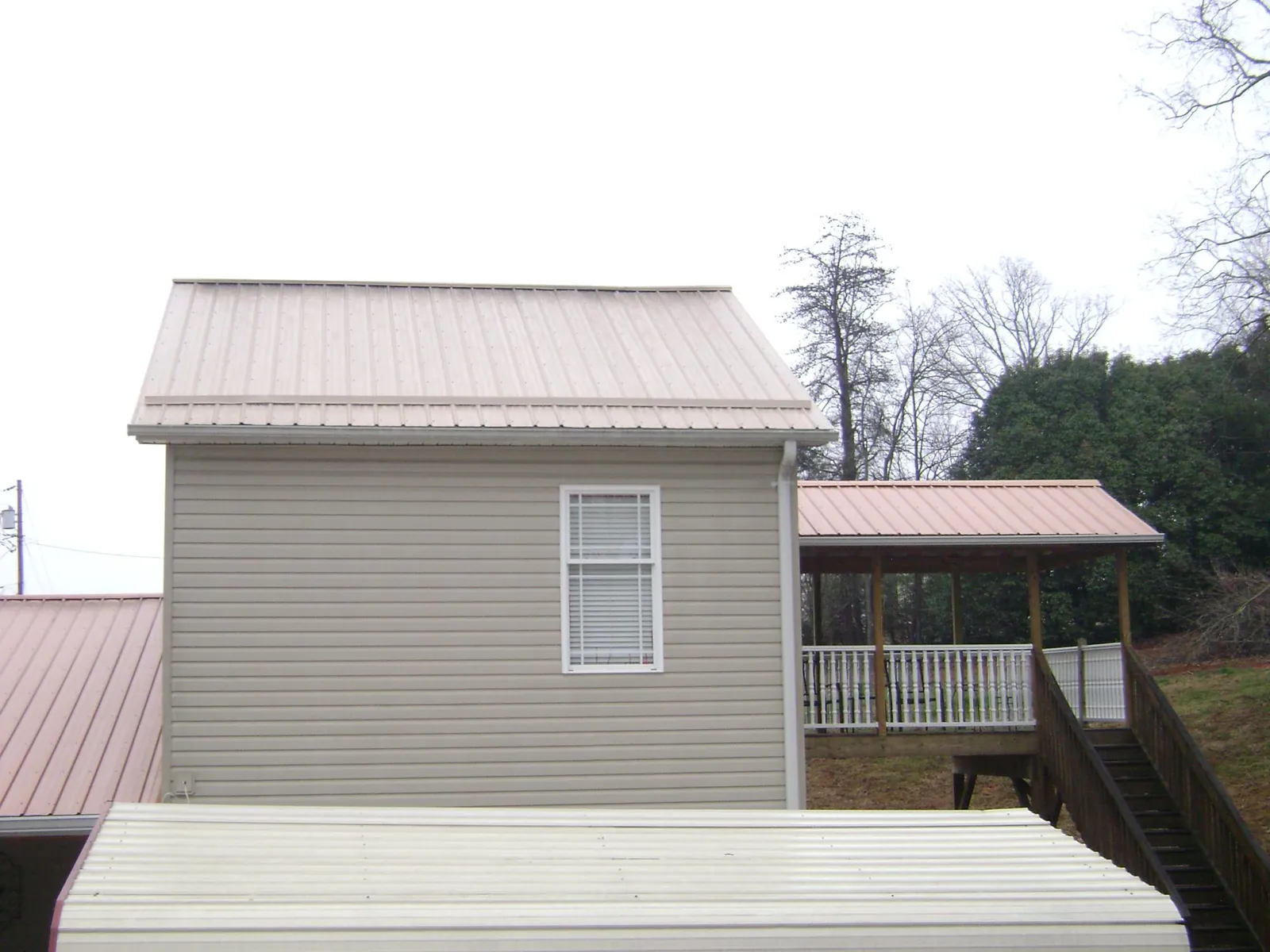 Tan metal roofs on a two story addition and attached porch, from a Roof Replacement job in Fayette